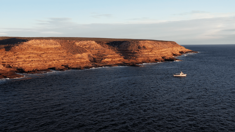 Reefwalker boat sailing along Kalbarri’s rugged coastline at sunset with golden cliffs in the distance